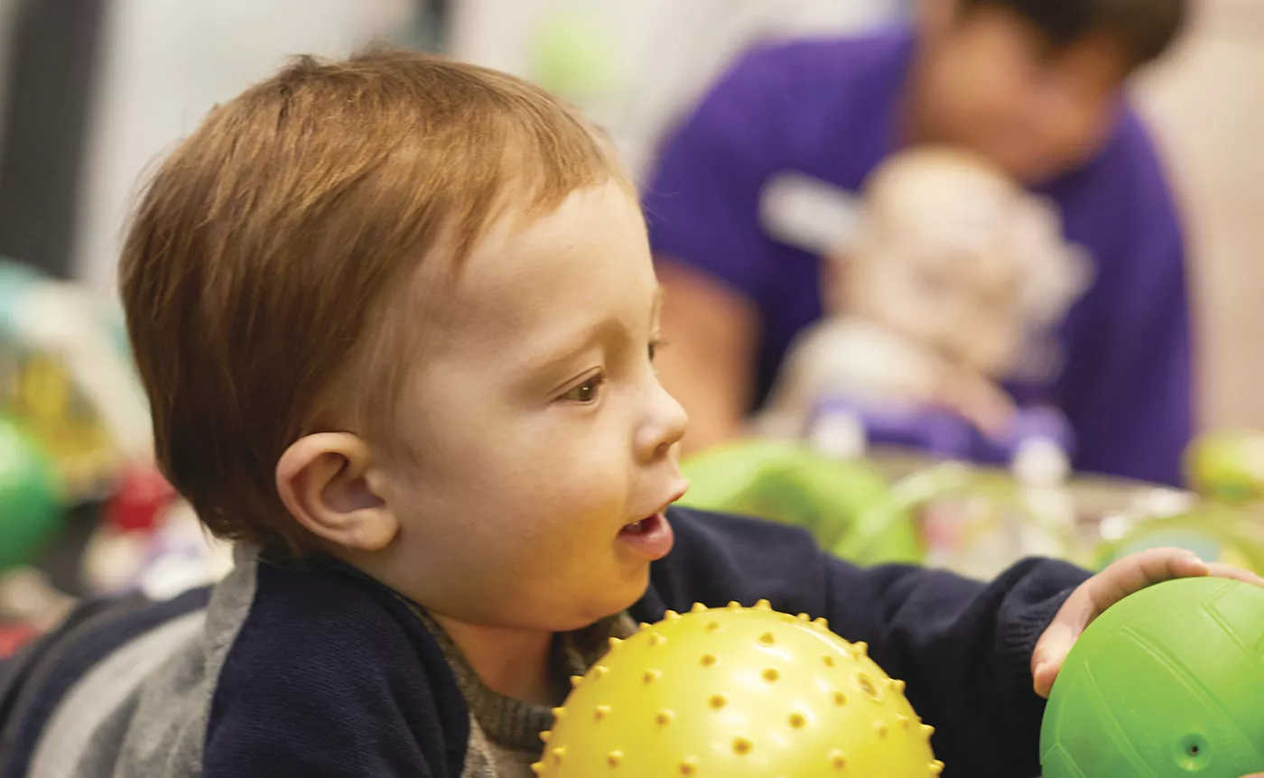 Young child playing with a ball with YMCA staff in the background