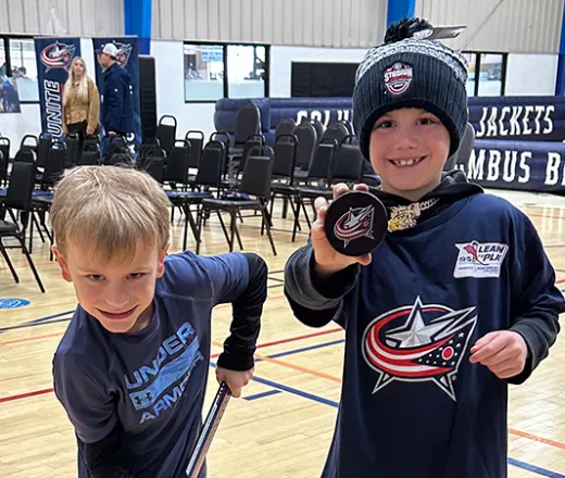 Two children with Columbus Blue Jackets gear smiling in a gym
