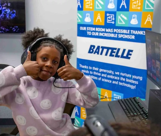 student smiles with thumbs up in front of a Battelle sign