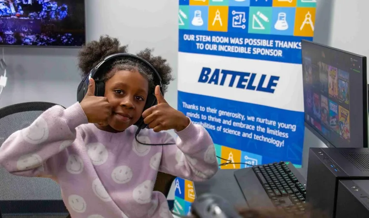 student smiles with thumbs up in front of a Battelle sign