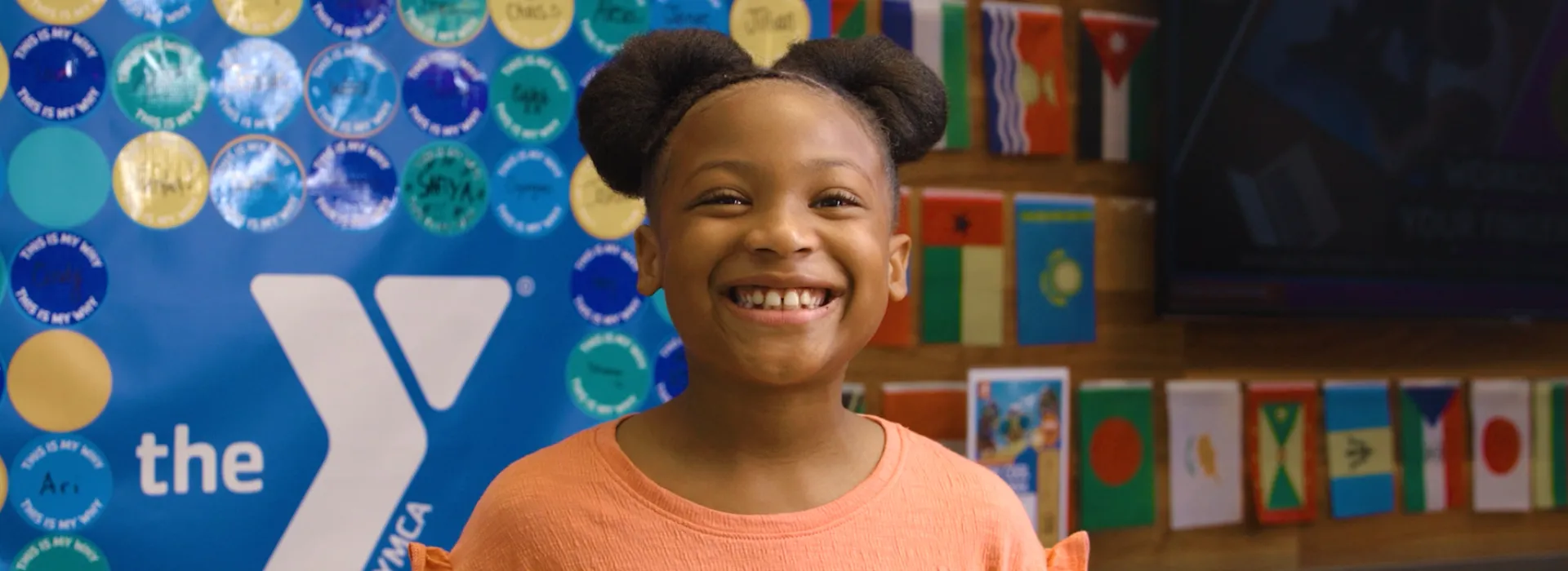 A youth smiling in front of YMCA poster board